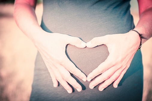 Pregnant woman's stomach with hands in a shape making a heart.