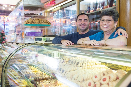 A photo of a middle aged mother and her son behind the counter of a family-owned pastry shop.