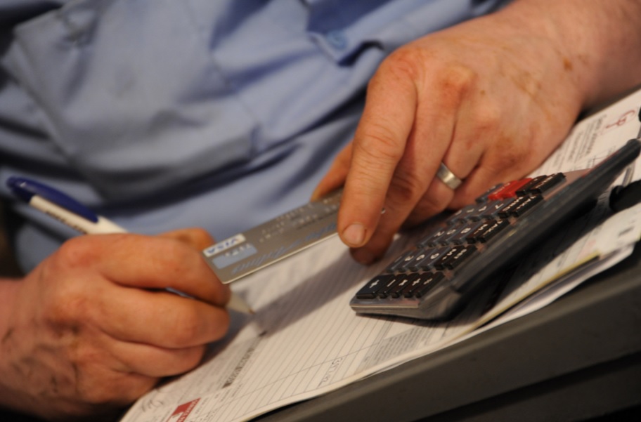 An older man holds a credit card and calculates his financials and writes them down