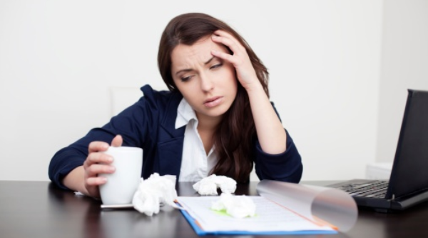 A sick woman sitting at work with tissues scattered on her desk.