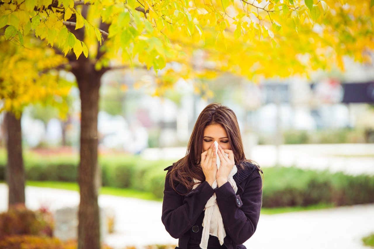 Woman blowing her nose in front of trees