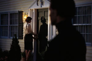 A man watching a woman enter her home from the shadows.